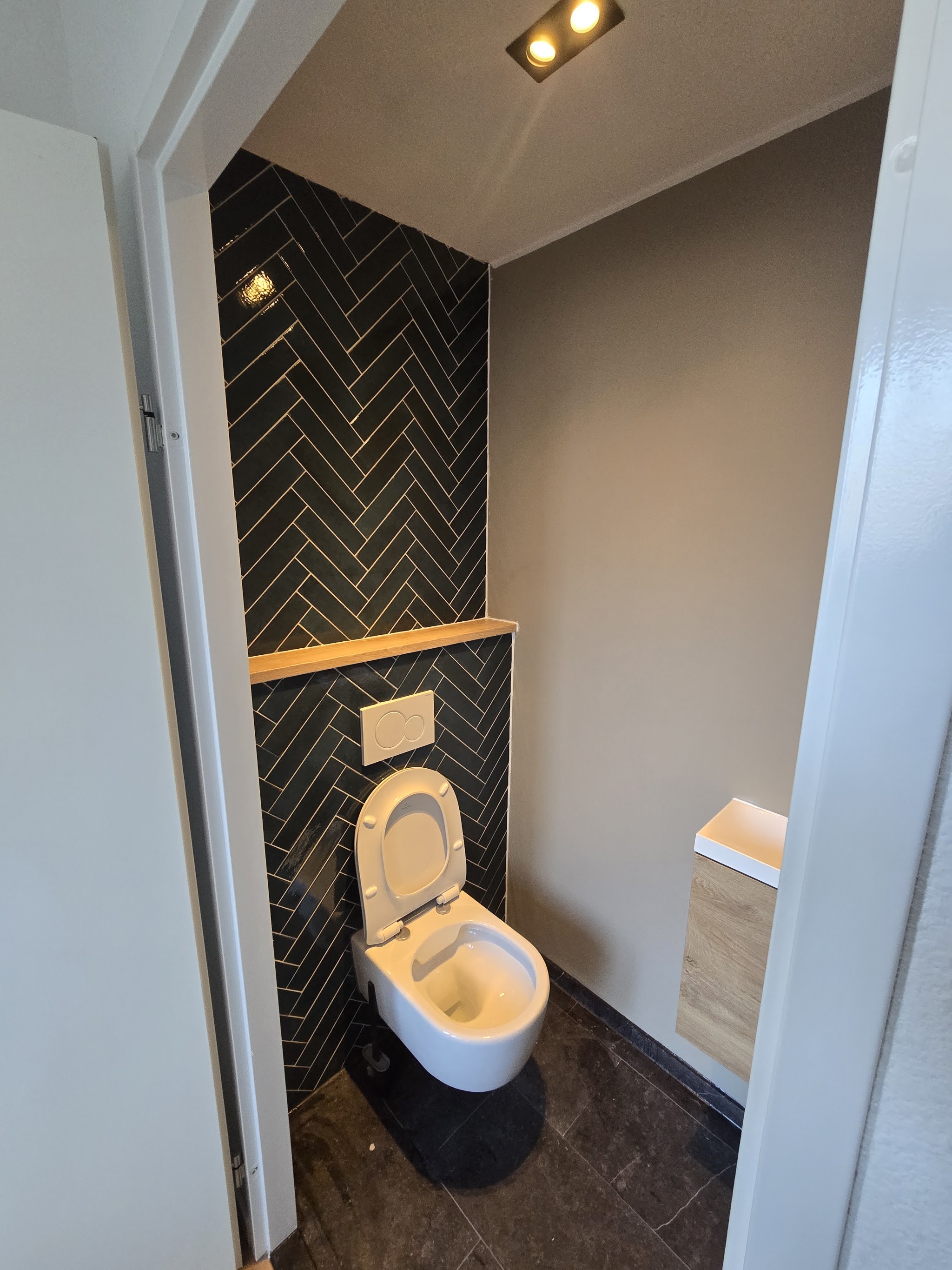 Toilet met donkergroene visgraattegels, zwevend toilet en houten plank