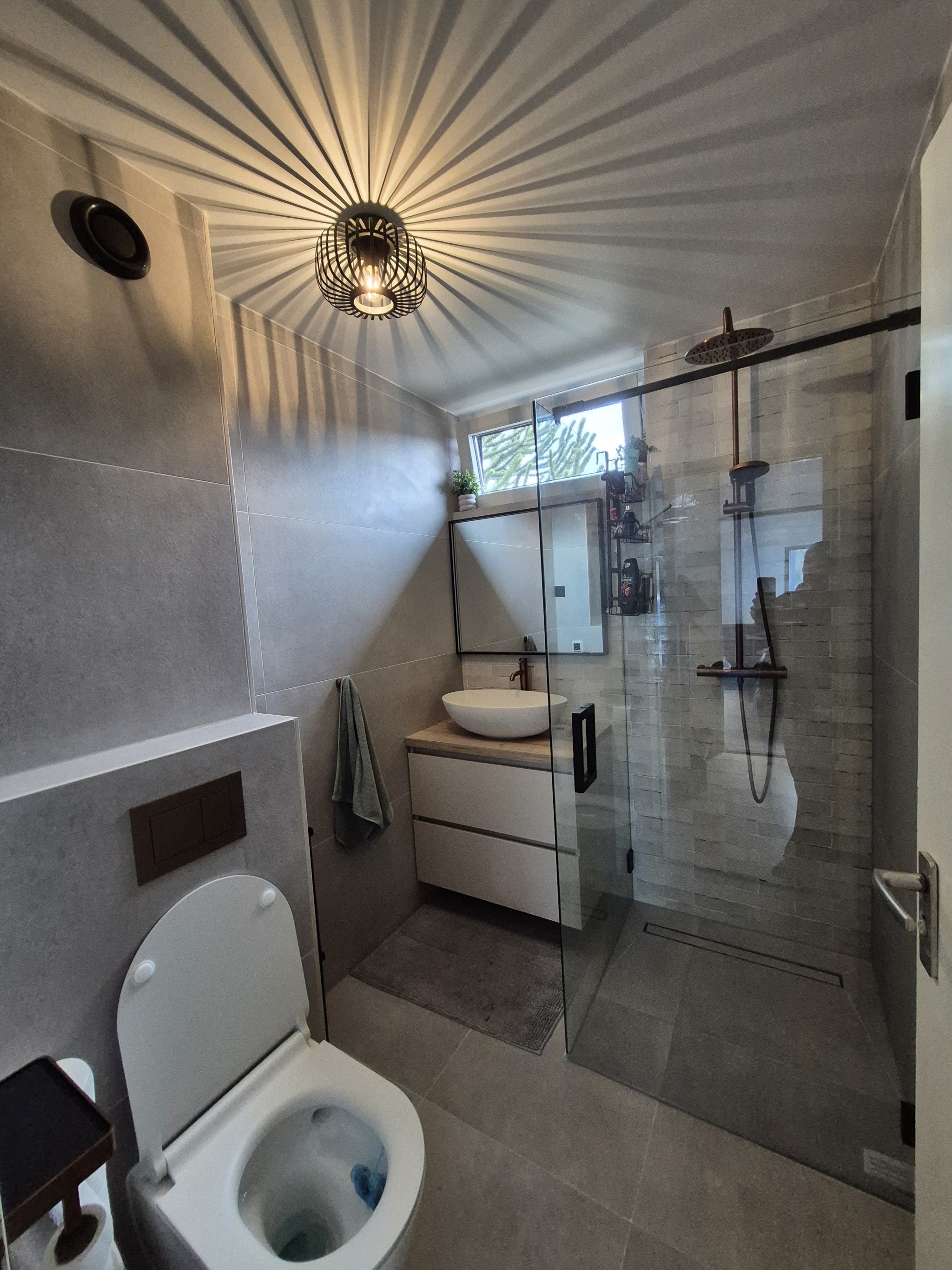 Badkamer met inloopdouche achter glas, zwarte kranen en zwevend toilet